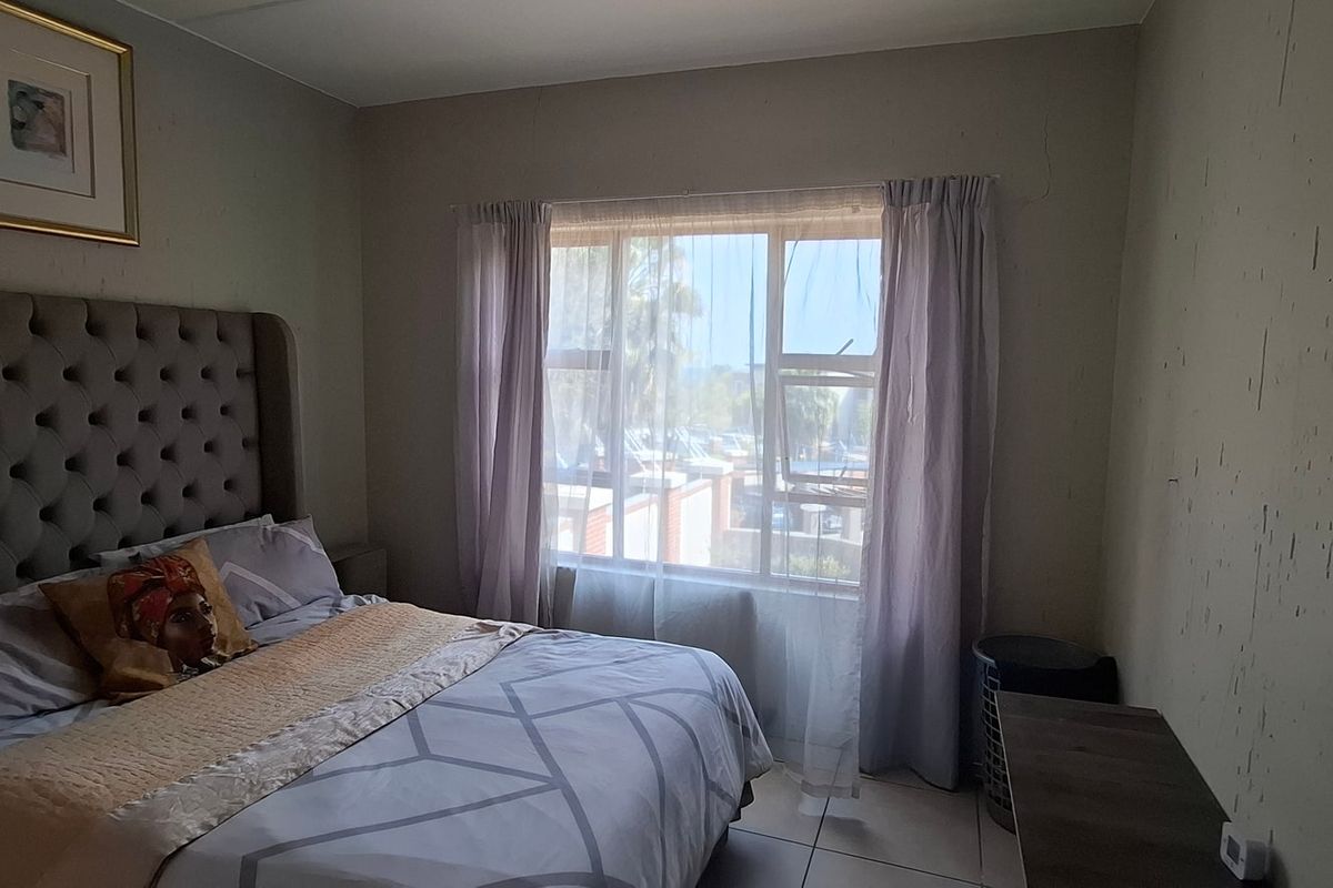 A bedroom featuring tiled flooring and a large window, currently showing signs of wall surface wear and plaster cracking.