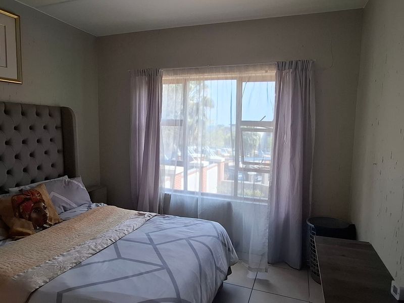 A bedroom featuring tiled flooring and a large window, currently showing signs of wall surface wear and plaster cracking.