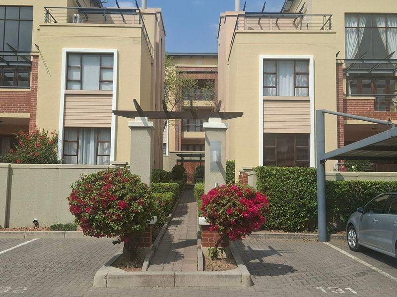 Front view of a modern apartment complex featuring paved parking, a covered carport, and a landscaped pedestrian entrance with a pergola.