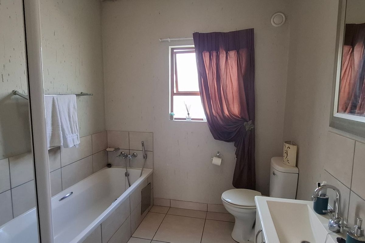 A functional bathroom featuring a bathtub, toilet, and vanity basin with neutral wall and floor tiling.