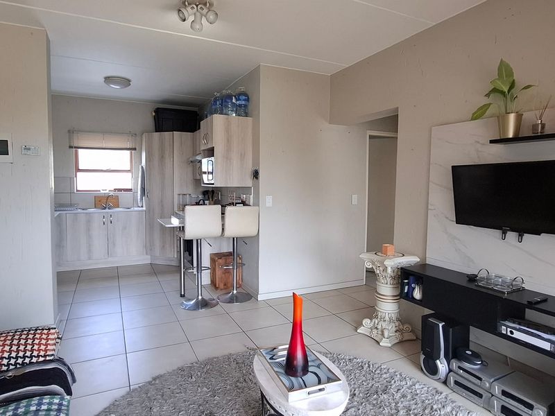 Open-plan living area featuring tiled flooring, a compact kitchen with built-in cabinetry, and a dedicated media wall unit.