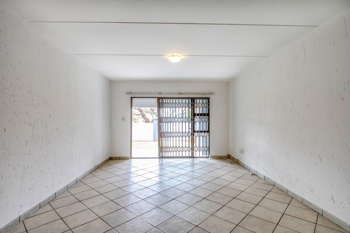 An empty, open-plan living area featuring tiled flooring, textured walls, and a sliding glass door with a security gate leading to the exterior.