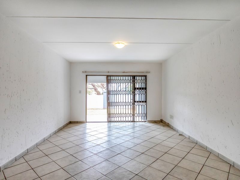 An empty, open-plan living area featuring tiled flooring, textured walls, and a sliding glass door with a security gate leading to the exterior.