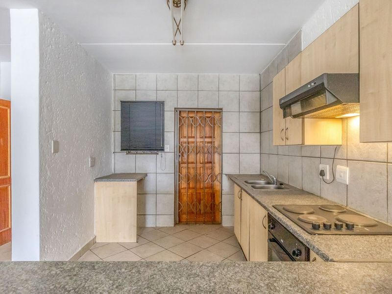 A functional kitchen featuring built-in cabinetry, laminate countertops, an electric hob with extractor fan, and tiled finishes throughout.