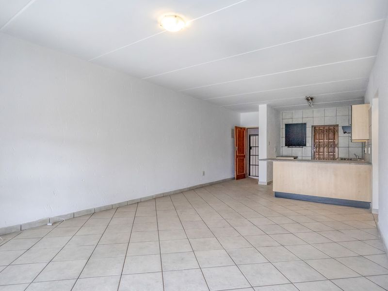 An open-plan living and kitchen area featuring tiled flooring, a breakfast bar, and functional kitchen cabinetry in a neutral, vacant space.
