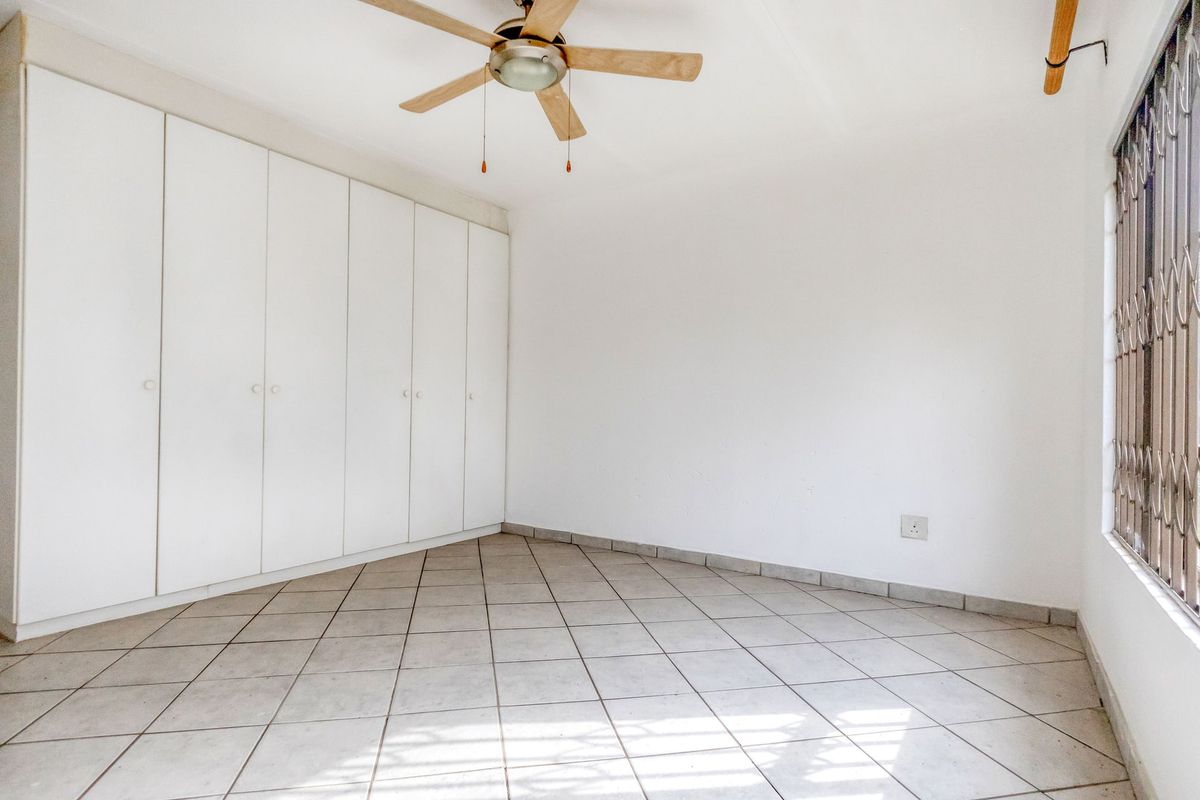 An empty bedroom featuring tiled flooring, built-in cupboards, and a ceiling fan, providing a clean and neutral space ready for personalization.