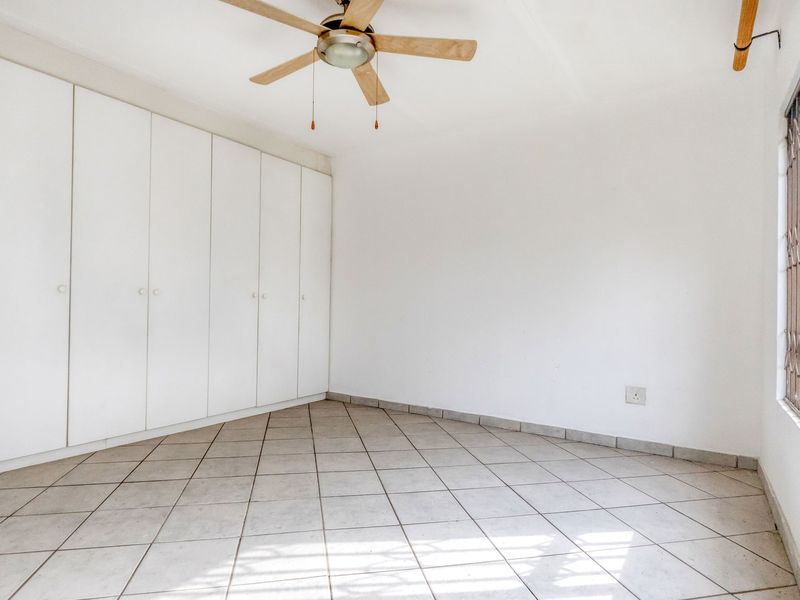 An empty bedroom featuring tiled flooring, built-in cupboards, and a ceiling fan, providing a clean and neutral space ready for personalization.