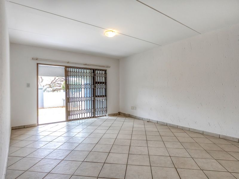 An empty, open-plan living area featuring neutral tiled flooring and a sliding glass door with a security gate leading to an outdoor space.