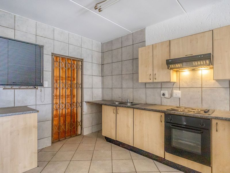 A functional kitchen featuring built-in cabinetry, laminate countertops, an integrated oven and hob, and tiled splashbacks with a security gate entrance.