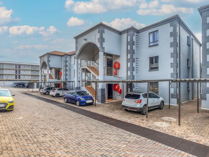 Exterior view of a multi-story apartment complex featuring covered parking bays, paved driveway, and external staircases providing access to units.