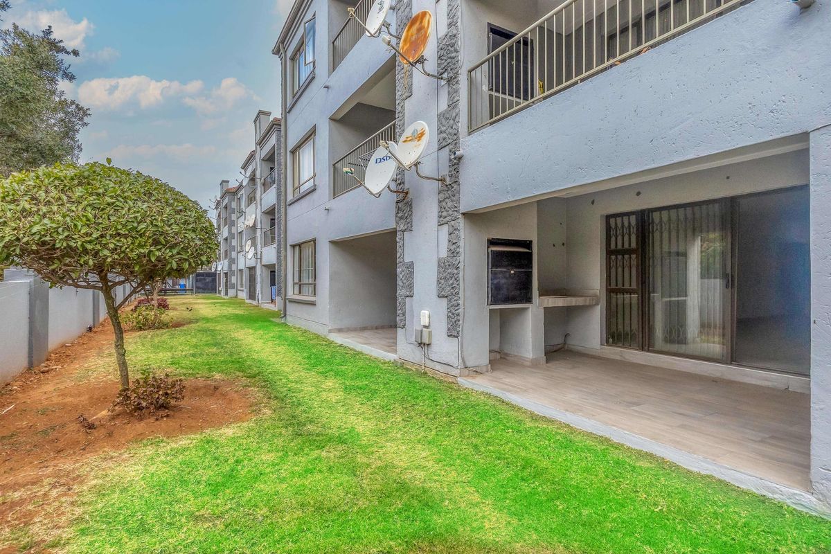 Rear view of the apartment complex featuring ground floor patios with built-in braais, metal balustrades, and access to a communal garden area.