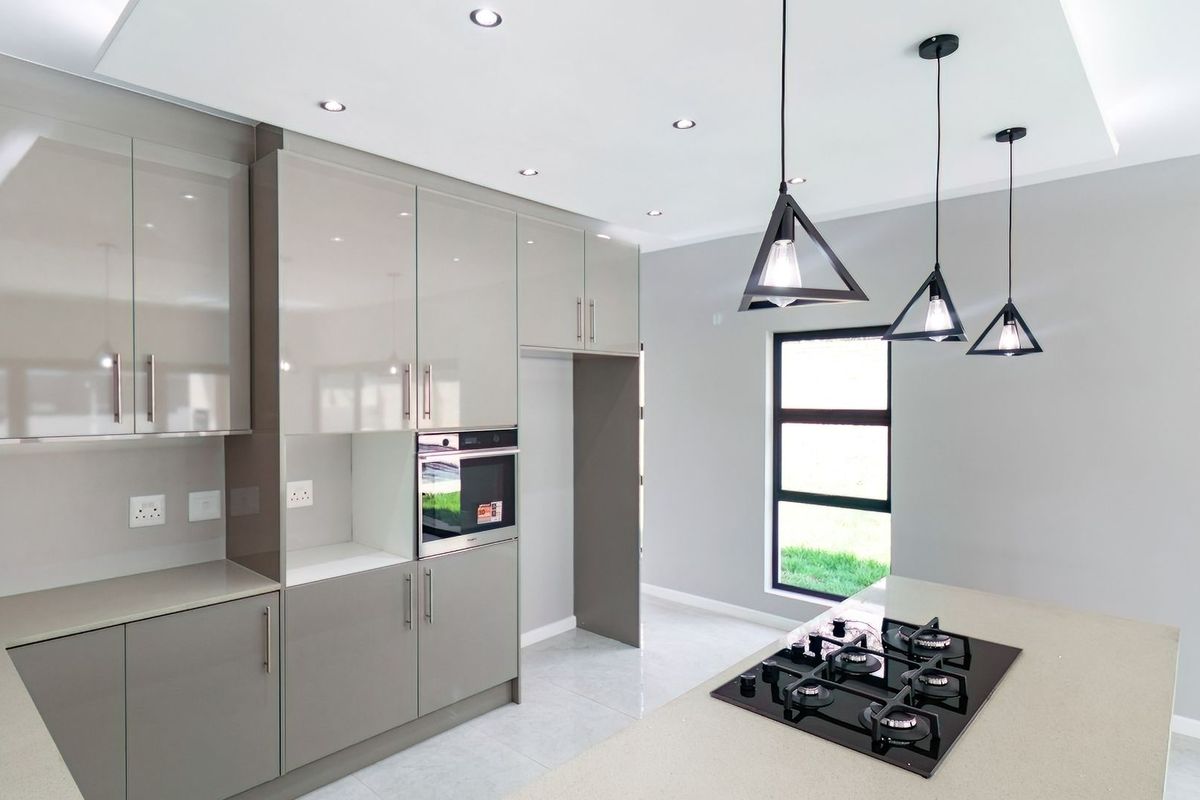 Modern kitchen featuring high-gloss cabinetry, stone countertops, a built-in oven, and a gas hob on a central island with contemporary pendant lighting.