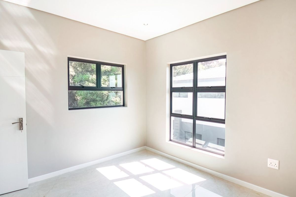 A bright, neutral-toned bedroom featuring modern tiled flooring, clean finishes, and large aluminium-framed windows that allow for ample natural light.