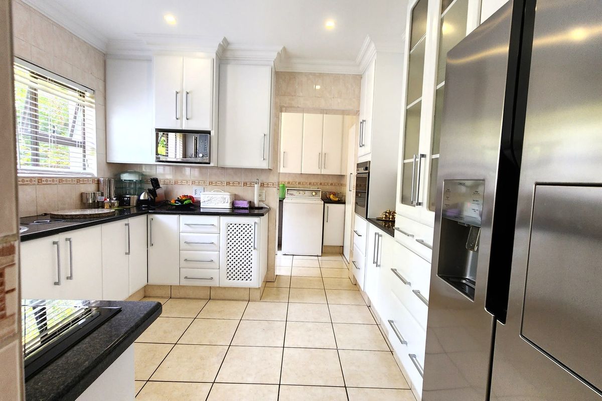 A well-maintained kitchen featuring white cabinetry, granite countertops, integrated appliances, and ceramic tile flooring, with an adjacent laundry area.