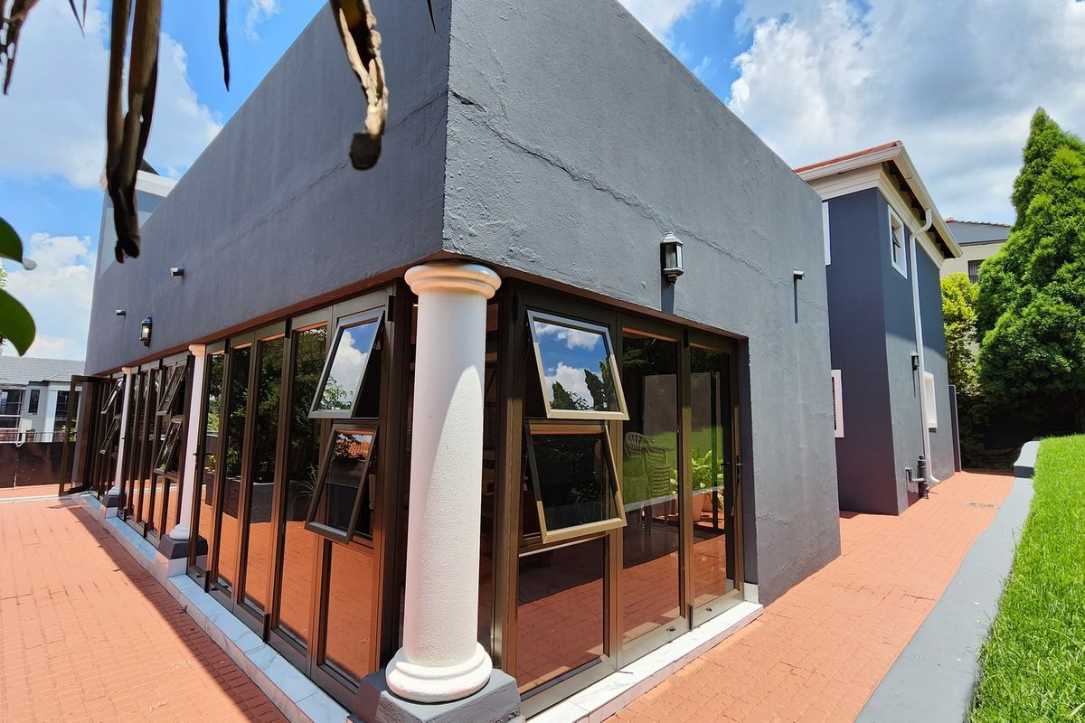 Rear exterior view featuring a modern dark-painted facade, extensive folding glass doors, and a brick-paved patio area.