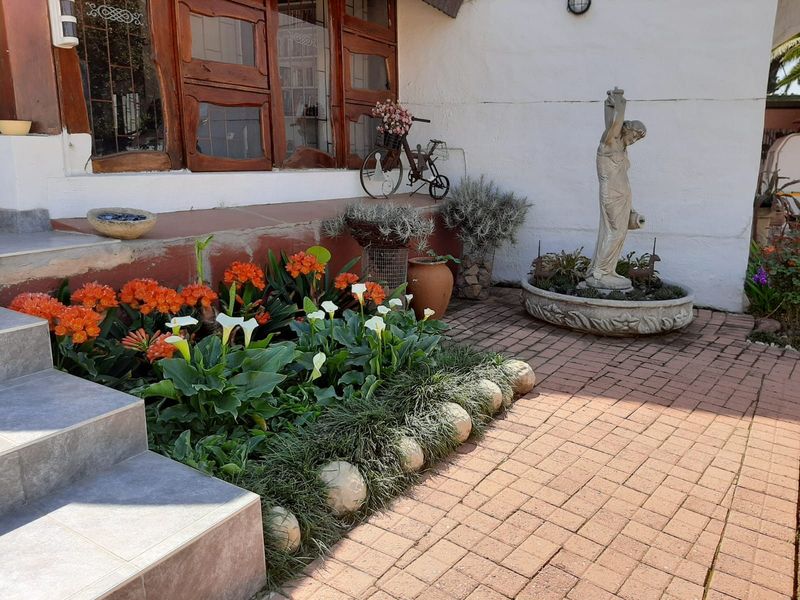 A landscaped garden area featuring a stone statue, paved walkway, and tiered steps leading to the main house entrance.