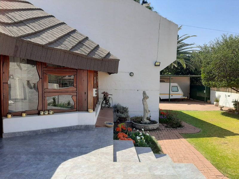 A rear view of the property featuring a tiled patio area, landscaped garden, paved walkway, and a covered carport structure.
