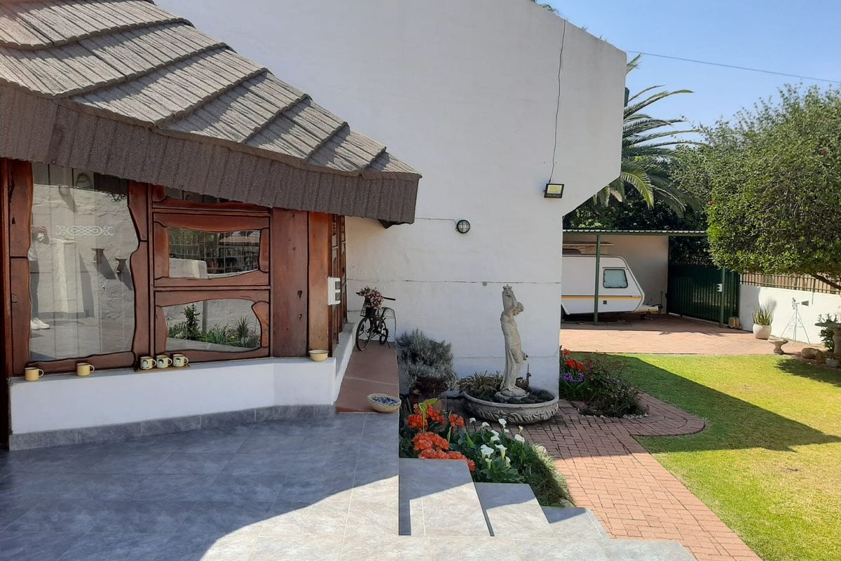 A rear view of the property featuring a tiled patio area, landscaped garden, paved walkway, and a covered carport structure.
