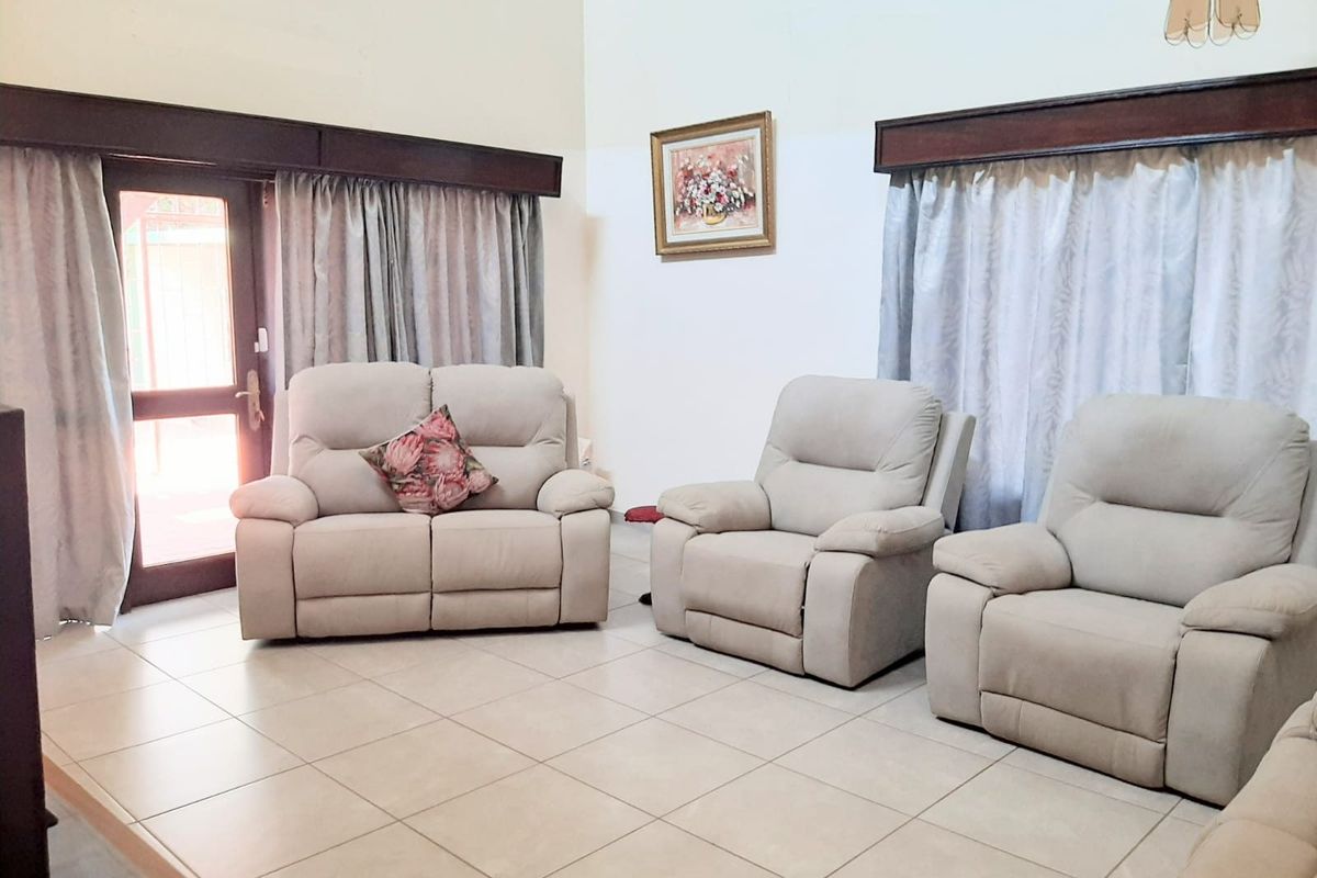 A spacious living room featuring neutral floor tiles, high ceilings, and direct access to an outdoor area through a glass-paneled door.