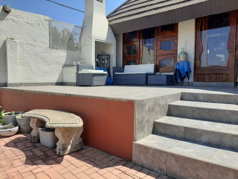 A raised patio area featuring tiled flooring, a built-in fireplace, and steps leading down to a paved garden space.