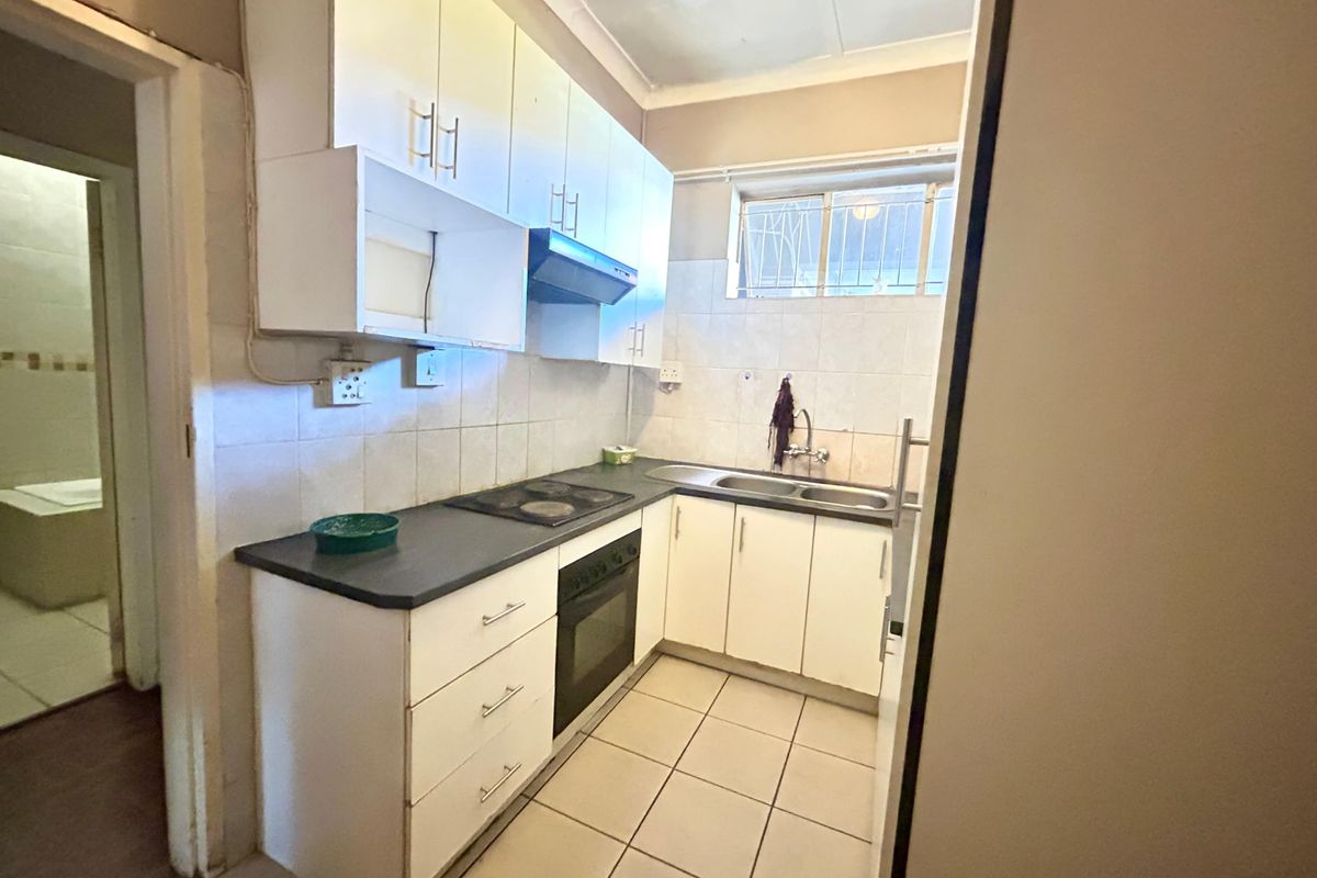 A functional kitchen featuring built-in cabinetry, an electric hob, oven, extractor fan, and a double sink with tiled splashbacks and flooring.