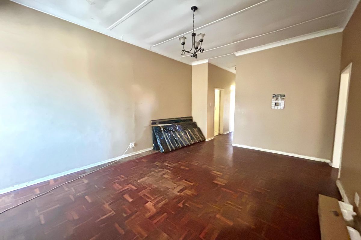 An empty living room featuring original parquet flooring, coved cornicing, and a central pendant light fitting, awaiting cosmetic updates and refurbishment.