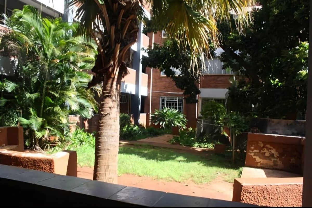 A view of the rear garden area featuring a brick apartment facade, a tiled patio, and a built-in braai facility.