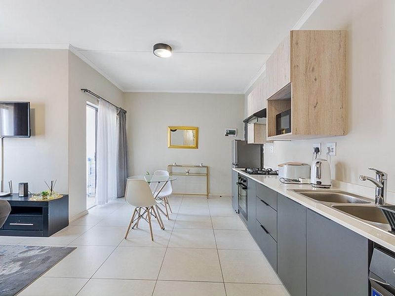 Modern open-plan kitchen and dining area featuring sleek cabinetry, gas hob, built-in oven, and tiled flooring with direct access to a balcony.