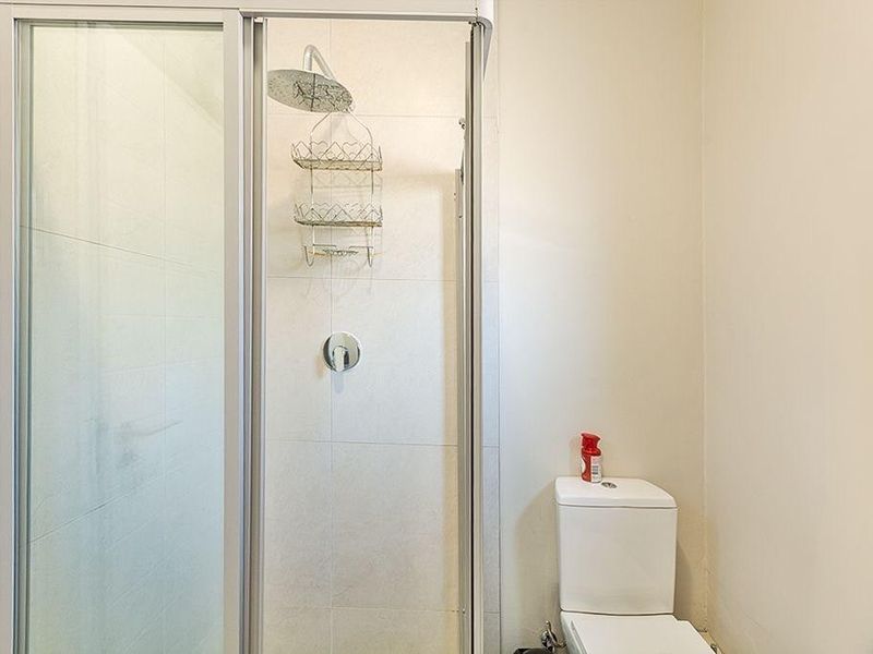 A functional bathroom featuring a glass-enclosed shower with a rain shower head and a standard white toilet.