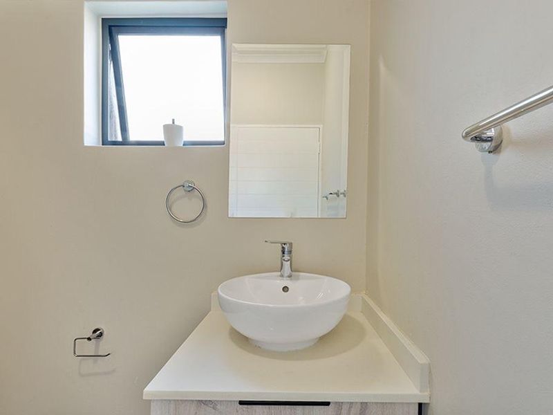 A clean and modern bathroom featuring a white vessel sink set on a vanity cabinet, complemented by a wall-mounted mirror and chrome fixtures.