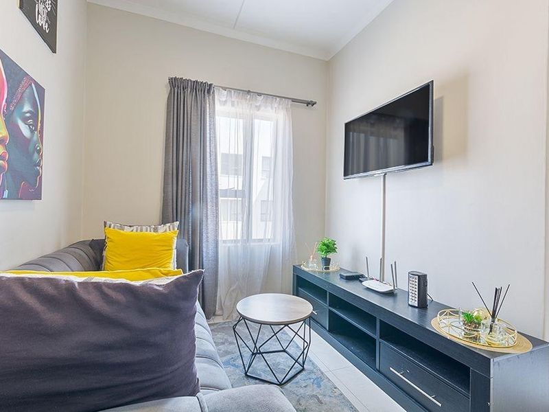 A compact living room featuring tiled flooring, a window with curtain treatments, and a wall-mounted television setup.