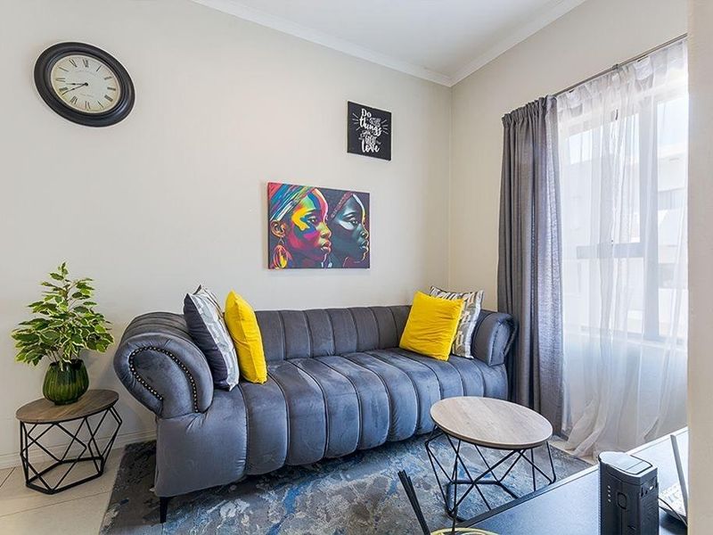 A well-maintained living room featuring neutral wall tones, tiled flooring, and a large window with curtain treatments.