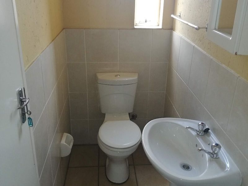 A compact bathroom featuring a pedestal basin, toilet, tiled flooring, and partial wall tiling, requiring cosmetic updates to the wall finishes.