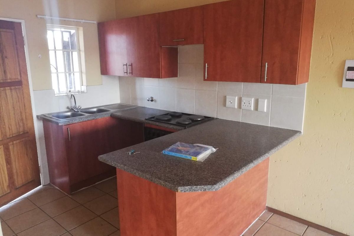 Functional kitchen featuring laminate cabinetry, a built-in electric hob, double bowl sink, and tiled splashback with a breakfast counter.