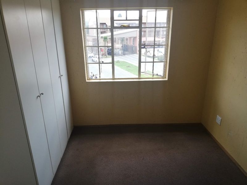An empty bedroom featuring built-in cupboards, carpeted flooring, and a grid-pane window overlooking the complex grounds.