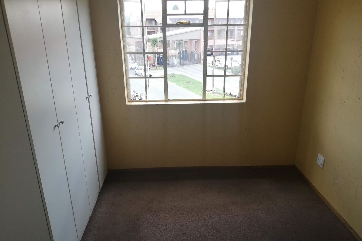 An empty bedroom featuring built-in cupboards, carpeted flooring, and a grid-pane window overlooking the complex grounds.