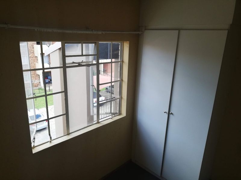 A compact bedroom featuring a built-in wardrobe and a steel-framed window overlooking the apartment complex grounds.
