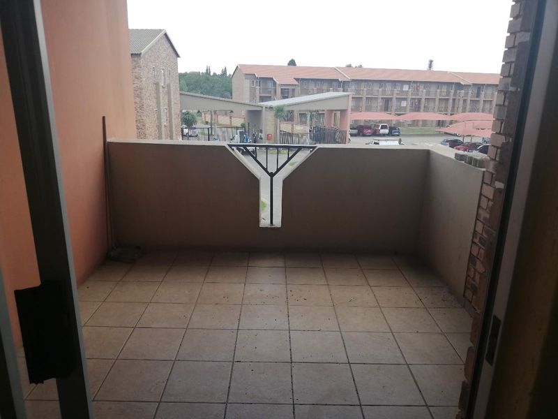 A private balcony featuring tiled flooring and a masonry balustrade with a metal insert, overlooking the apartment complex grounds.