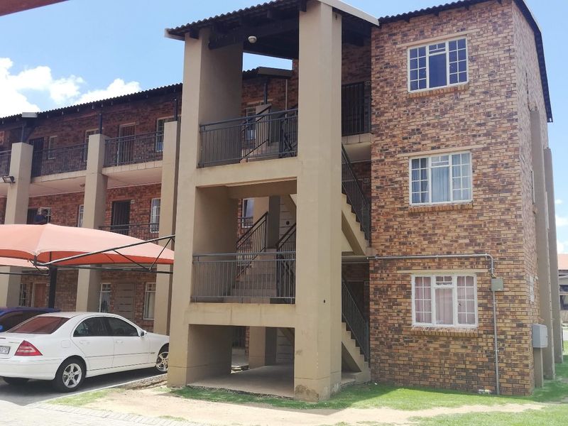 Exterior view of a multi-story apartment complex featuring face brick construction, external staircases, and dedicated carport parking.