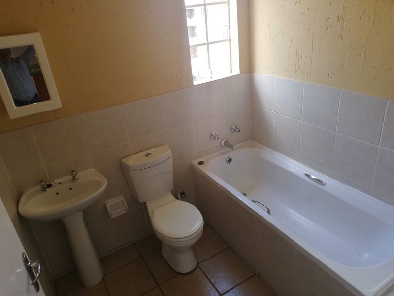 A functional bathroom featuring a pedestal basin, toilet, and bathtub with tiled finishes, requiring cosmetic updates to improve its overall aesthetic appeal.
