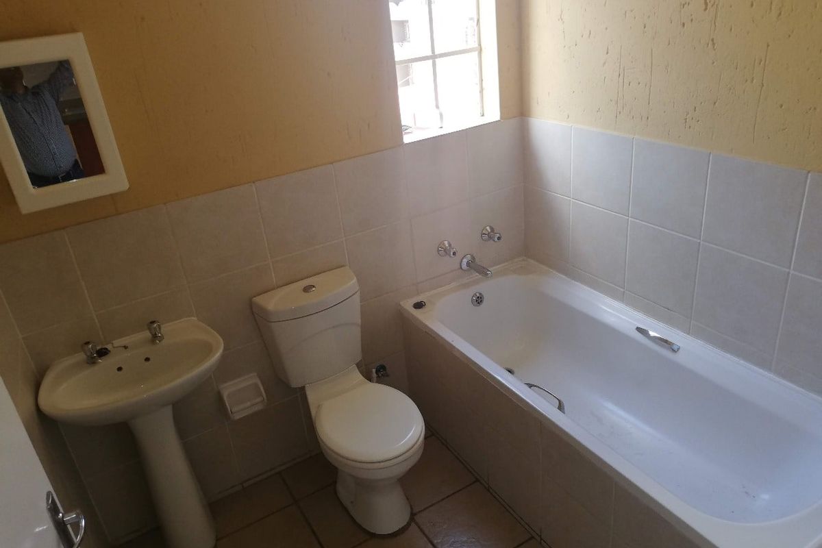 A functional bathroom featuring a pedestal basin, toilet, and bathtub with tiled finishes, requiring cosmetic updates to improve its overall aesthetic appeal.