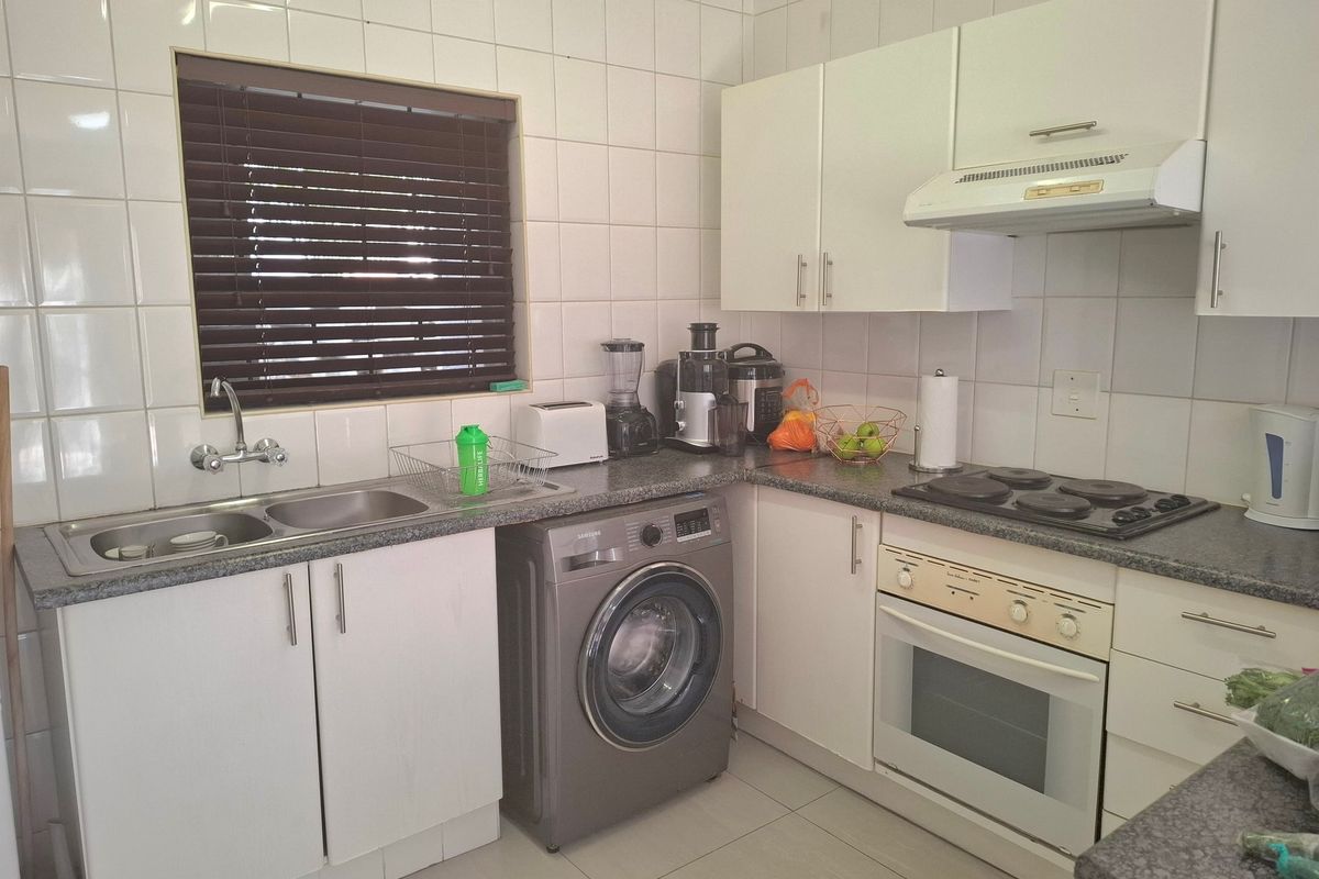 A functional kitchen featuring white cabinetry, tiled splashbacks, a built-in oven with hob, and space for a washing machine.