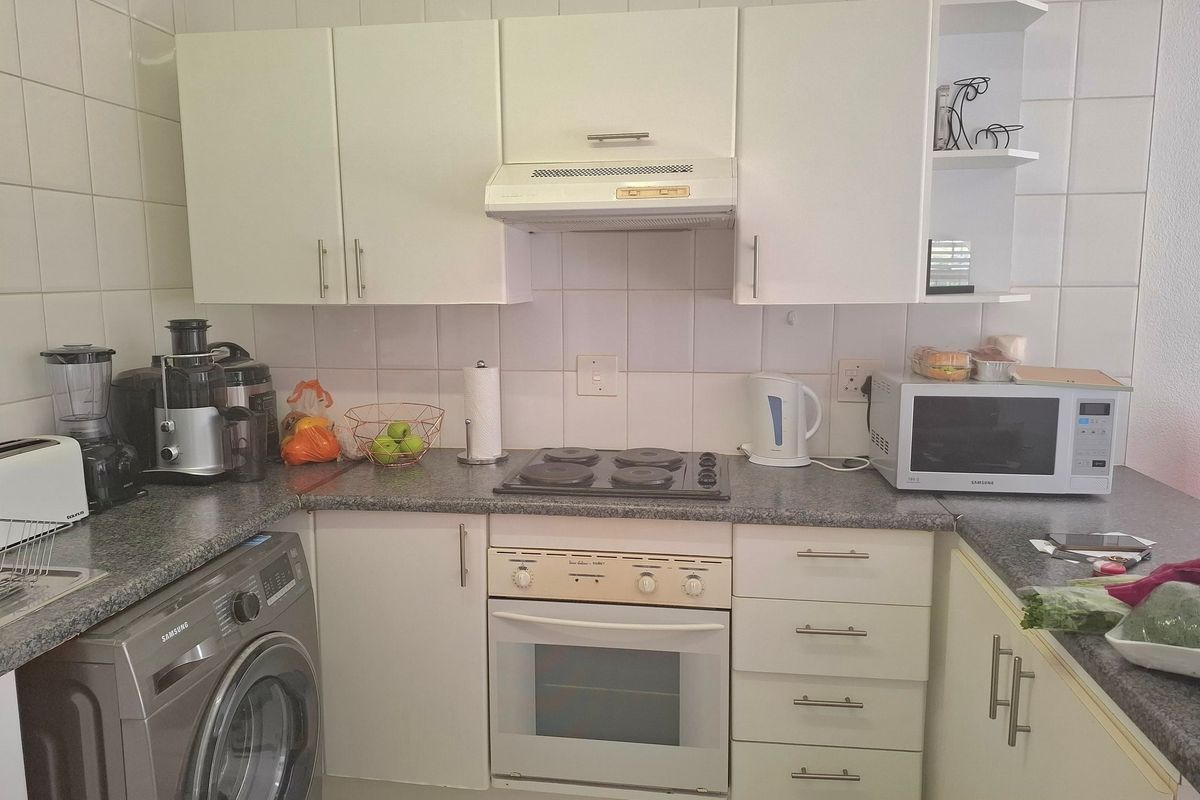 Compact kitchen featuring white cabinetry, tiled splashbacks, a built-in oven with electric hob, and dedicated space for a washing machine.