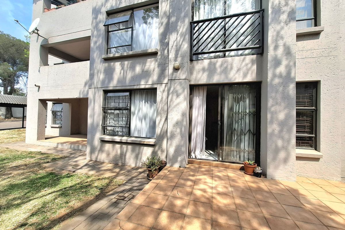 Rear view of the apartment building featuring a tiled patio area, sliding glass doors with security gates, and upper-level balcony access.