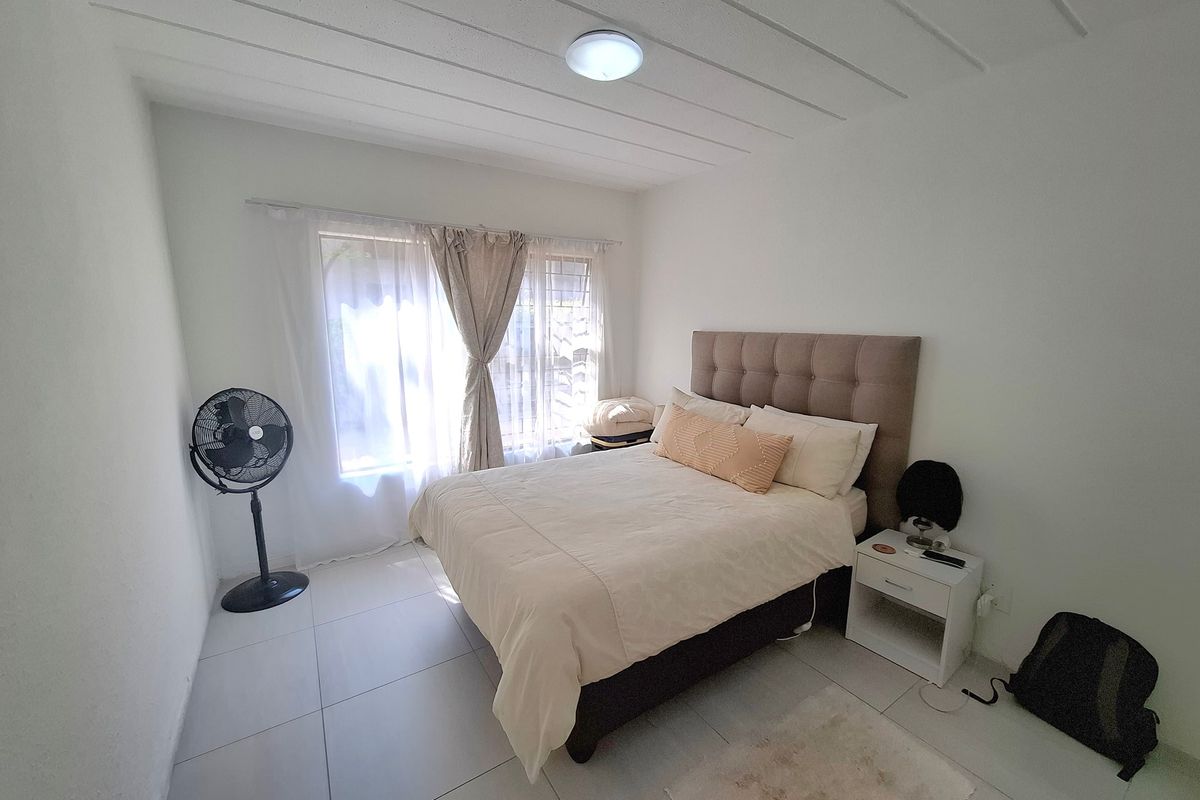 A functional bedroom featuring tiled flooring, a ceiling light fixture, and a window fitted with security bars.