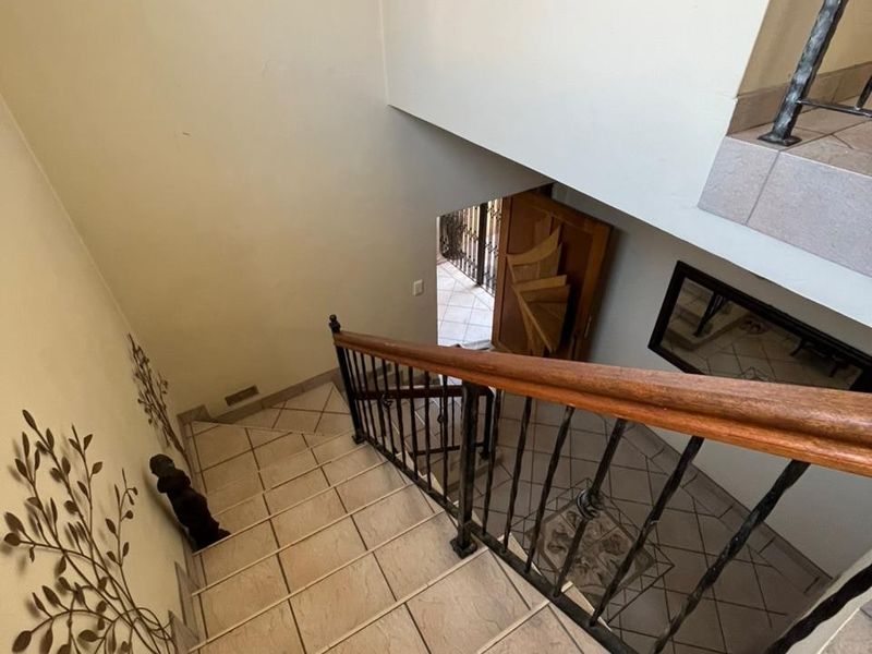 A staircase featuring tiled steps, a wrought iron balustrade with a wooden handrail, leading down to the main entrance area.