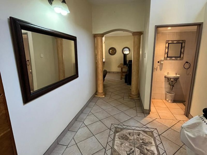 A tiled hallway featuring decorative columns, an arched entryway, and a convenient guest bathroom, leading towards the living area and staircase.