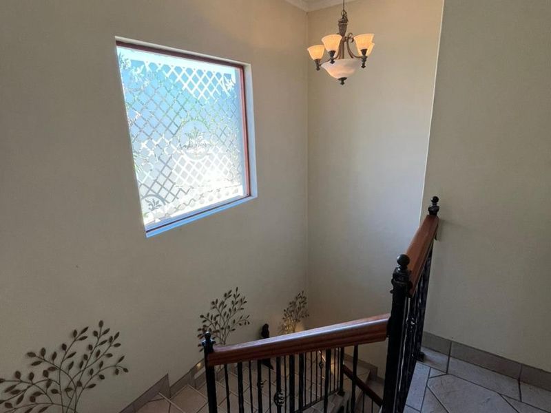 A bright staircase landing featuring a wrought iron balustrade with a wooden handrail, tiled flooring, and a decorative window.