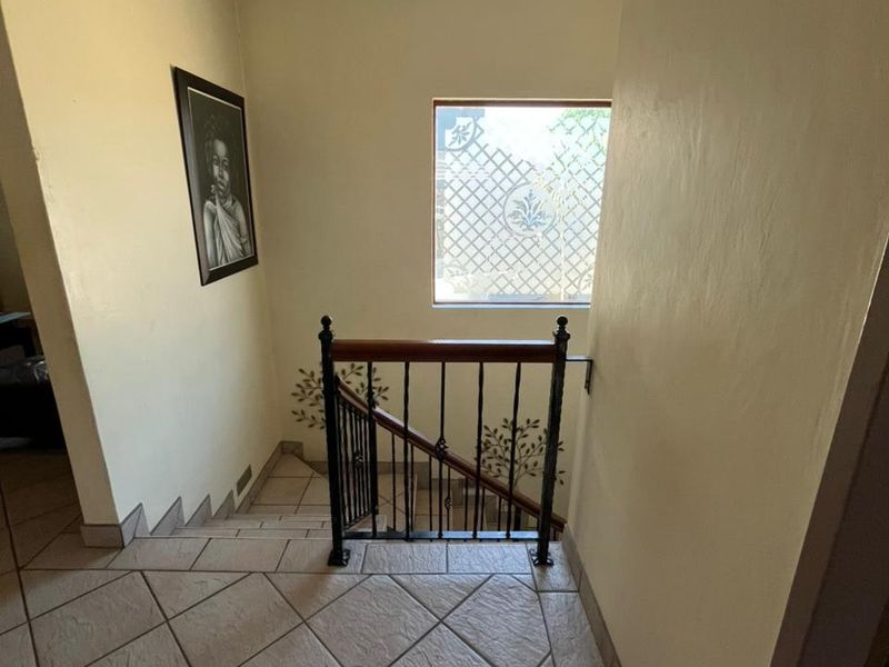 A bright hallway featuring a tiled staircase with a decorative wrought iron balustrade and wooden handrail, leading to a landing with a patterned window.