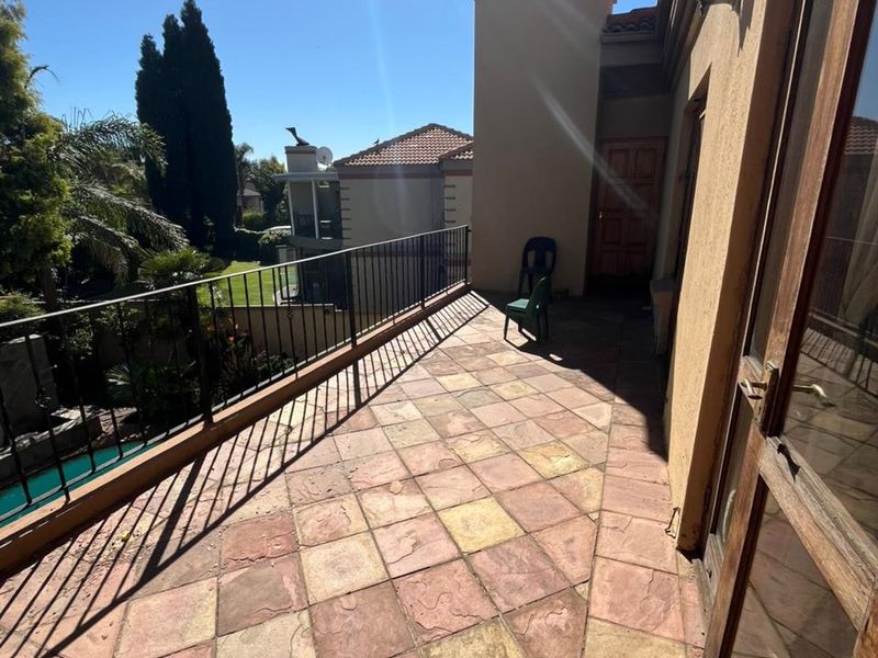 A spacious outdoor balcony featuring stone tile flooring, metal safety railings, and direct access to the home, overlooking the garden and pool area.